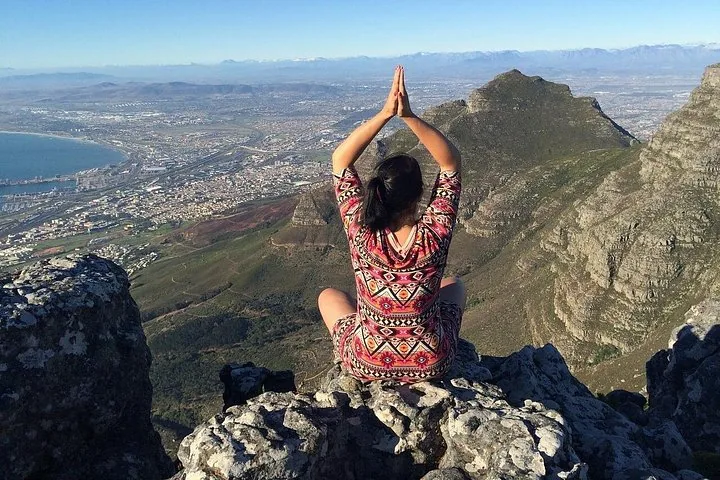 Eine Person, die Yoga auf einem felsigen Gipfel mit Blick auf die Stadt macht.